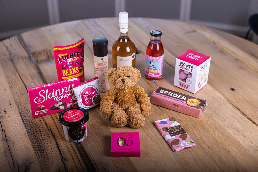 En smukt præsenteret  af produkter til en gavekurv til en pige-barnedåb, fyldt med lyserøde produkter og en kær bamse